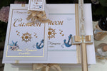 Christening Box with anchor and starfish designs, gold text and ribbon, and candle on a white background.