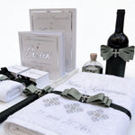 White towels with decorative ribbons, a bottle of wine, and baptism certificate folder on a white background