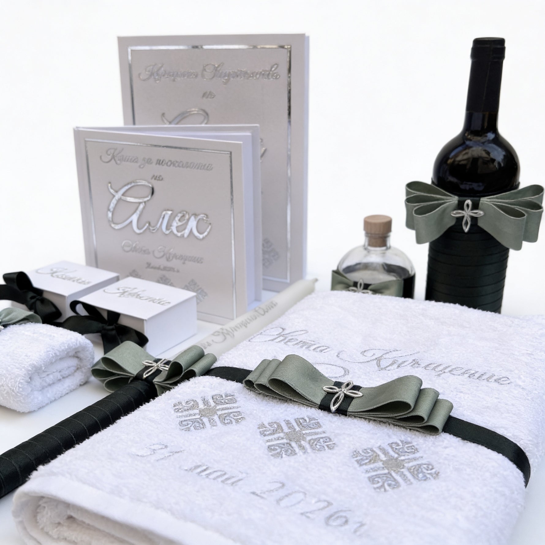 White towels with decorative ribbons, a bottle of wine, and baptism certificate folder on a white background