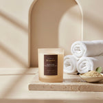 Candle hammam spa  on a stone surface next to rolled towels and a bowl of sand in a spa-like setting.