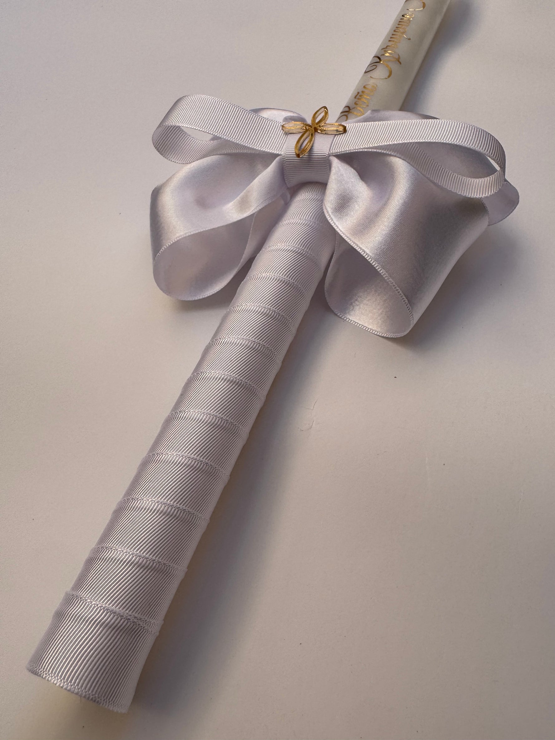 lose up of white satin and grosgrain bow with a gold cross on a christening candle
